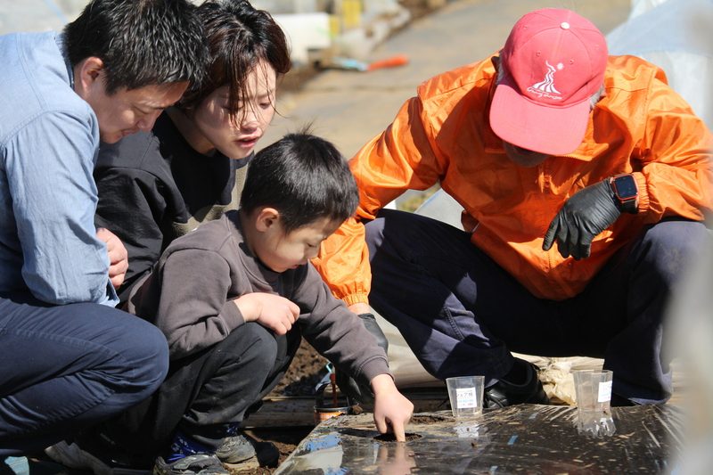 大人と子どもが菜園アドバイザーと一緒に、畑に種をまいている様子